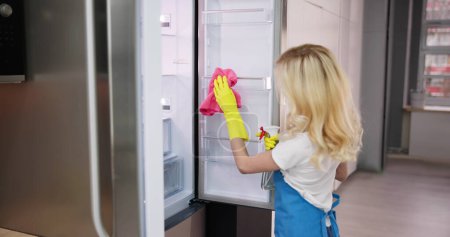 Photo for Young Smiling Professional Cleaning Service Woman Cleaning Refrigerator In Kitchen - Royalty Free Image