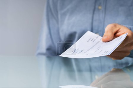 Photo for Close-up Of A Human Hand Giving Cheque On Desk - Royalty Free Image