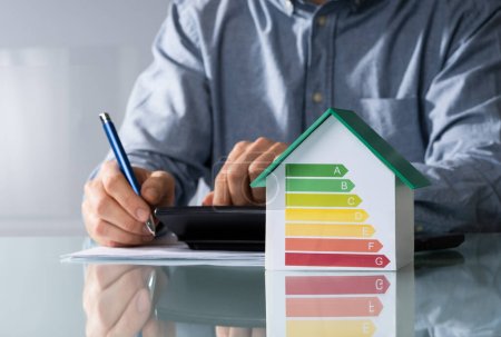 Foto de Midsection del hombre de negocios que calcula la factura con el gráfico de eficiencia energética en el modelo de la casa en la oficina - Imagen libre de derechos