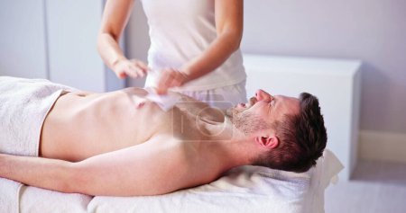 Photo for Man Waxing Chest With Wax Strip In Spa - Royalty Free Image