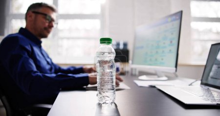 Foto de Botella de agua en el escritorio y el hombre en segundo plano usando la computadora - Imagen libre de derechos