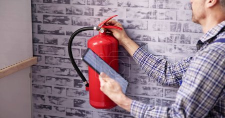 Foto de Trabajador Instalando extintor de incendios. Servicio de Inspección. Comprobación de la etiqueta de seguridad - Imagen libre de derechos