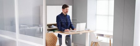 Foto de Soporte de escritorio de altura ajustable en la oficina con computadora - Imagen libre de derechos