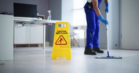 Téléchargez les photos : Section basse de plancher de nettoyage de concierge masculin avec la prudence Wet Floor Sign In Office - en image libre de droit