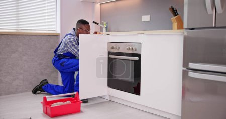 Téléchargez les photos : Réparateur en salopette Réparation Cabinet charnière dans la cuisine - en image libre de droit