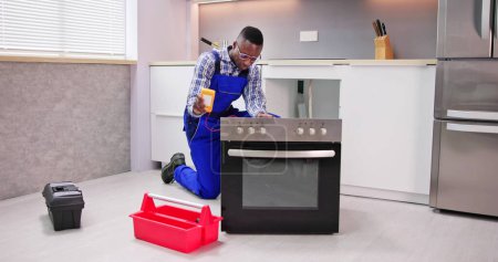Téléchargez les photos : Jeune réparateur masculin Réparation four dans la cuisine - en image libre de droit