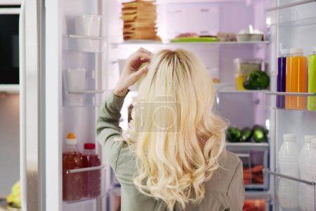 Téléchargez les photos : Femme affamée à la recherche de nourriture dans la cuisine à la maison - en image libre de droit