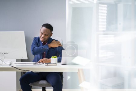 Téléchargez les photos : Jeune homme d'affaires ayant la douleur à l'épaule tout en travaillant au bureau de l'ordinateur au bureau - en image libre de droit