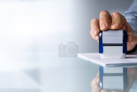 Foto de Primer plano de la mano de una persona sellando en el formulario de solicitud aprobado sobre el escritorio - Imagen libre de derechos