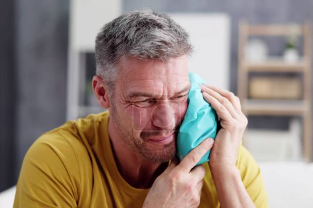 Photo for Upset Man Touching Cheek With Cold Water Bag At Home - Royalty Free Image