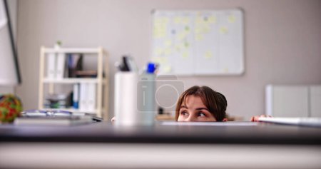 Photo for Scared Woman Hiding Behind Chair And Under Desk - Royalty Free Image