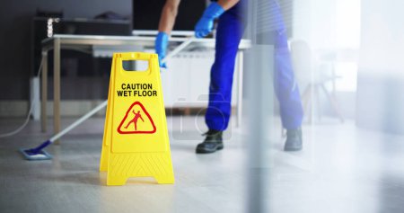 Photo for Low Section Of Male Janitor Cleaning Floor With Caution Wet Floor Sign In Office - Royalty Free Image