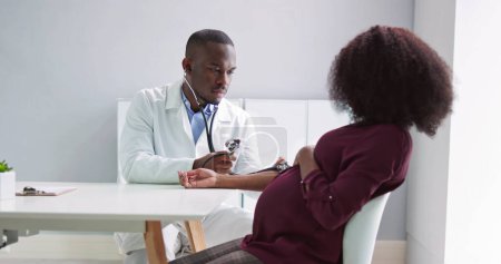 Téléchargez les photos : Male Doctor Measuring Blood Pressure Of Pregnant Woman In Clinic - en image libre de droit