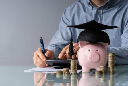 Photo for Close-up Of Piggy Bank Wearing Graduation Hat And Stacked Coins In Front Of Businessperson - Royalty Free Image