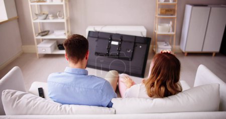 Foto de Hombre sentado en un sofá frente a la televisión caída con la pantalla rota - Imagen libre de derechos