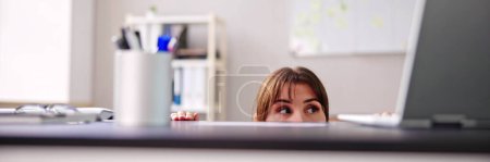 Une femme apeurée se cache derrière son fauteuil et sous son bureau