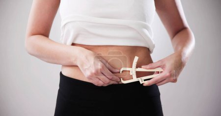 Foto de Manos femeninas que miden la grasa del vientre con calibrador de grasa - Imagen libre de derechos