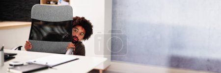 Photo for Scared Man Hiding Behind Office Desk In Room - Royalty Free Image