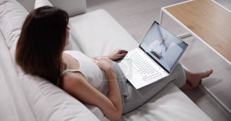 Photo for Pregnant Woman Lying On Sofa Video Conferencing With Doctor On Laptop - Royalty Free Image