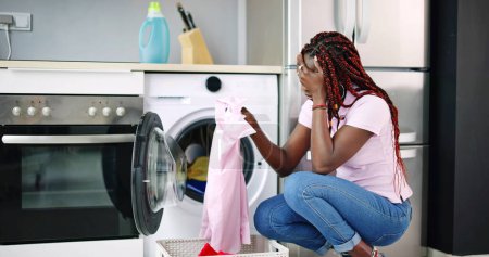 Téléchargez les photos : Jeune femme accroupi avec des vêtements nettoyés près de la laveuse électronique - en image libre de droit