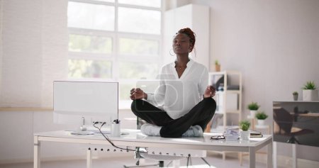 Téléchargez les photos : Un employé africain fait de la méditation de yoga en santé mentale au bureau - en image libre de droit