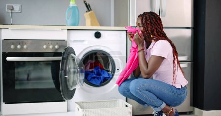 Téléchargez les photos : Jeune femme accroupi avec des vêtements nettoyés près de la laveuse électronique - en image libre de droit