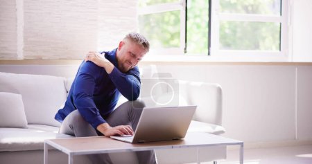 Mann arbeitet mit Schulterschmerzen und Entzündung am Laptop