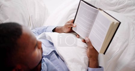 Foto de Feliz joven africano leyendo su libro sobre la cama - Imagen libre de derechos