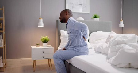 Téléchargez les photos : Homme assis sur le lit souffrant de douleurs au dos - en image libre de droit