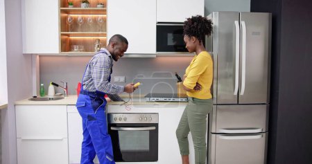 Foto de Hombre reparador instalación de cocina de inducción con la mujer de pie en la cocina - Imagen libre de derechos