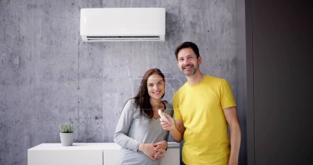 Foto de Feliz pareja joven que ajusta la temperatura del aire acondicionado por control remoto - Imagen libre de derechos