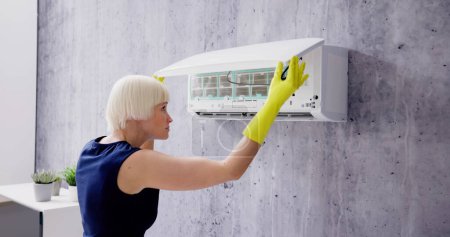 Téléchargez les photos : Jeune femme nettoyage système de climatisation à la maison - en image libre de droit
