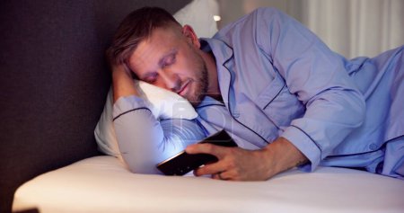 Foto de Hombre en la cama con teléfono móvil por la noche - Imagen libre de derechos
