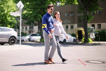Téléchargez les photos : Jeune femme aidant aveugle homme avec bâton blanc tout en traversant la route - en image libre de droit