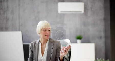 Téléchargez les photos : Jeune femme d'affaires utilisant la télécommande devant le climatiseur monté sur le mur - en image libre de droit