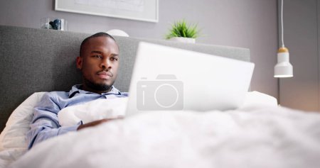 Téléchargez les photos : Happy Man assis sur le lit en utilisant un ordinateur portable - en image libre de droit