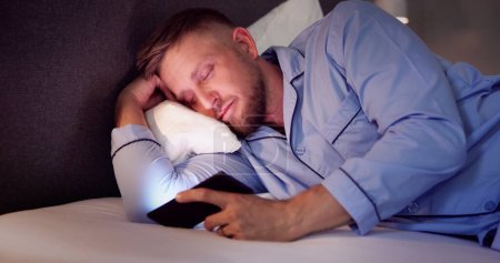 Téléchargez les photos : Homme au lit avec téléphone portable la nuit - en image libre de droit