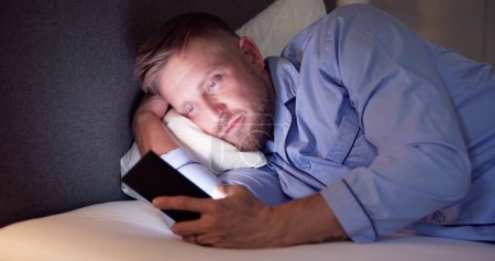 Téléchargez les photos : Homme allongé sur le lit en utilisant un téléphone portable la nuit - en image libre de droit