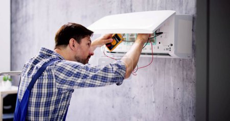 Téléchargez les photos : Portrait d'un technicien masculin mi-adulte testant le climatiseur avec le multimètre numérique - en image libre de droit