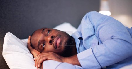 Téléchargez les photos : Jeune homme africain souffrant de fièvre allongée sur le lit - en image libre de droit