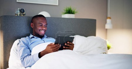Photo for Man Lying On Bed Looking At Illuminated Digital Tablet - Royalty Free Image