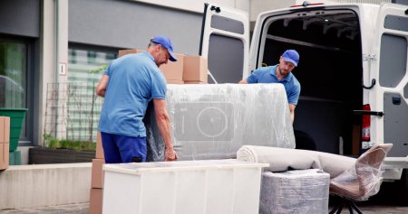 Photo for Male Workers In Blue Uniform Unloading Furniture From Truck - Royalty Free Image