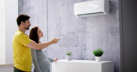 Glückliches junges Paar stellt Temperatur der Klimaanlage per Fernbedienung ein
