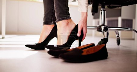 Téléchargez les photos : Businesswoman Changer de chaussures de talon haut à des chaussures confortables dans le bureau - en image libre de droit