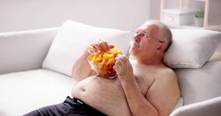 Téléchargez les photos : Rester assis à trop manger Mode de vie alimentaire. Les personnes en surpoids regardent la télévision - en image libre de droit