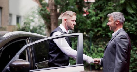 Téléchargez les photos : Homme donnant la clé de voiture au voiturier masculin près du panneau de stationnement de voiturier - en image libre de droit