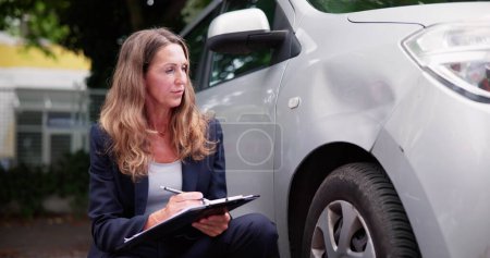 Photo for Insurance Agent Inspecting Damaged Car With Insurance Claim Form - Royalty Free Image