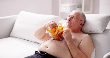 Téléchargez les photos : Rester assis à trop manger Mode de vie alimentaire. Les personnes en surpoids regardent la télévision - en image libre de droit