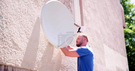 Foto de Joven Técnico Masculino en Uniforme Instalación de TV satélite plato en la pared - Imagen libre de derechos