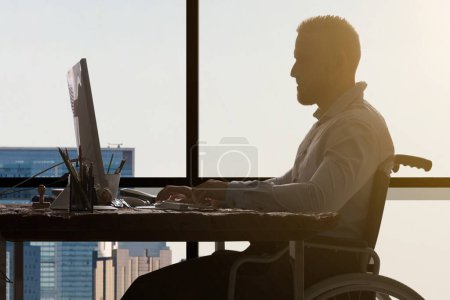 Foto de Empresario discapacitado sentado en silla de ruedas usando computadora en el lugar de trabajo - Imagen libre de derechos